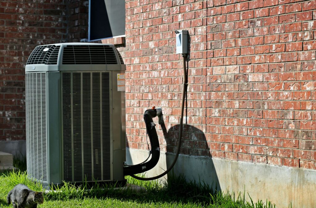 Outdoor air conditioning unit next to a brick wall with electrical connections.