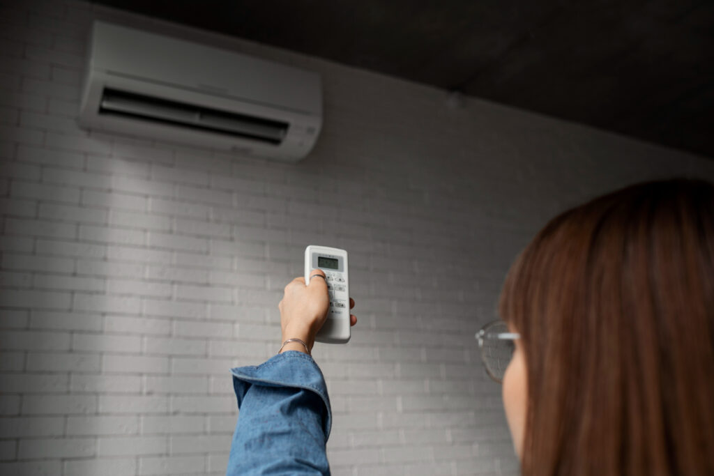 Person pointing a remote control at a wall-mounted air conditioner.