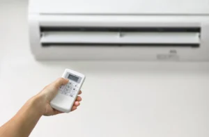 Hand holding a remote control pointed at a wall-mounted air conditioner