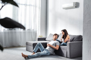 Two people sitting on a gray sectional sofa in a bright living room.