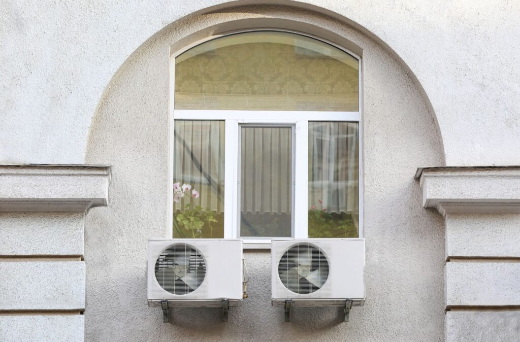 Two air conditioner outdoor units mounted on a building wall beneath a window.