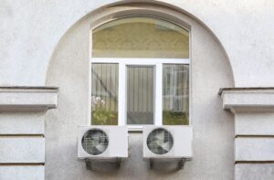 Two air conditioner outdoor units mounted on a building wall beneath a window.